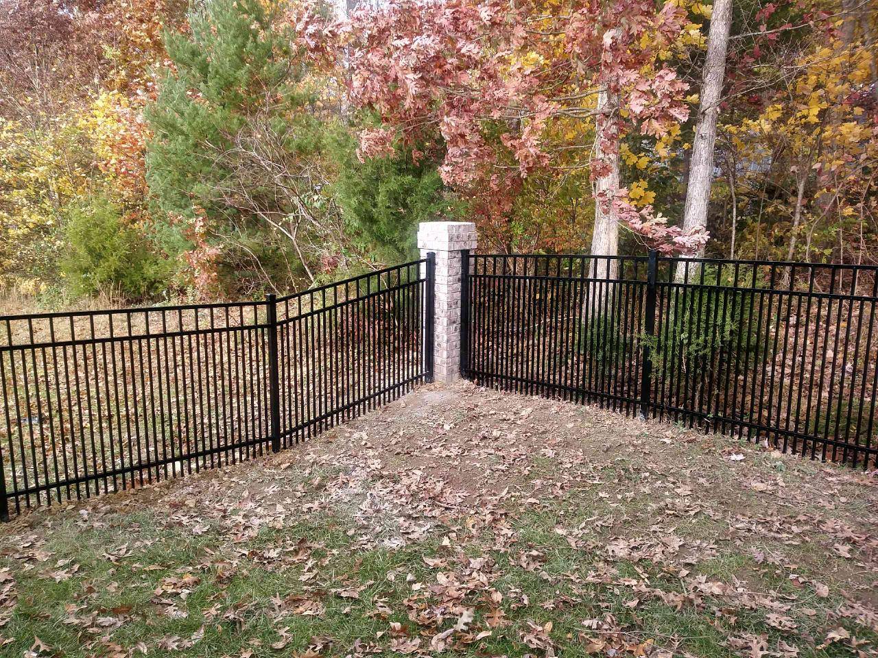 Black aluminum fence meeting a stone pillar at the edge of woods