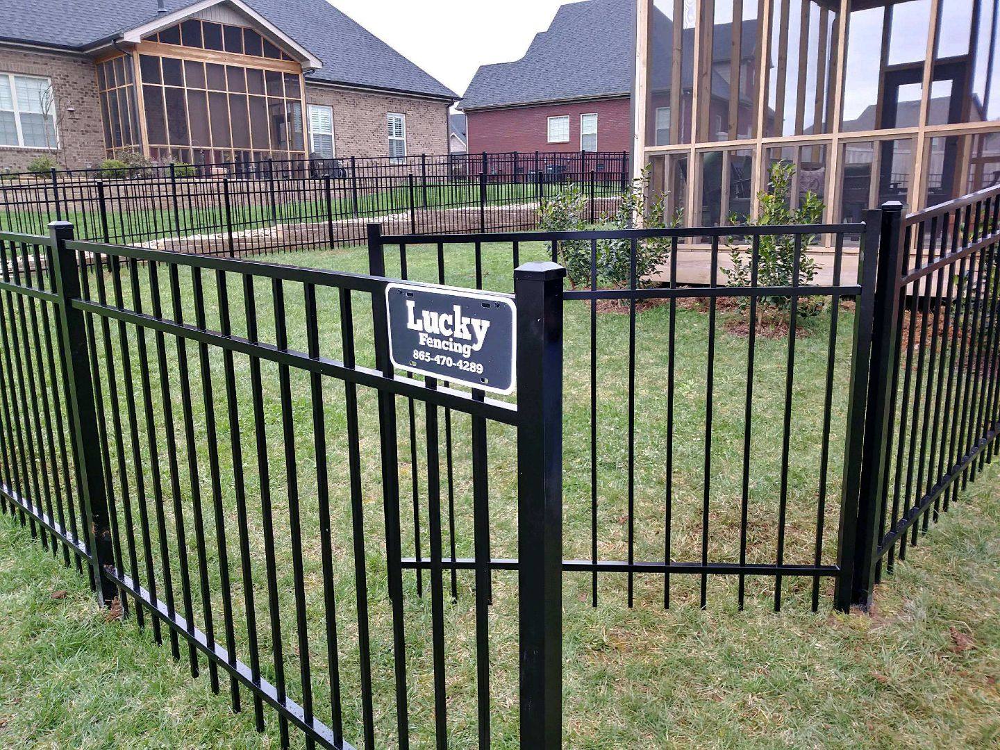 Black aluminum fence around a backyard with a Lucky Fencing sign on the gate