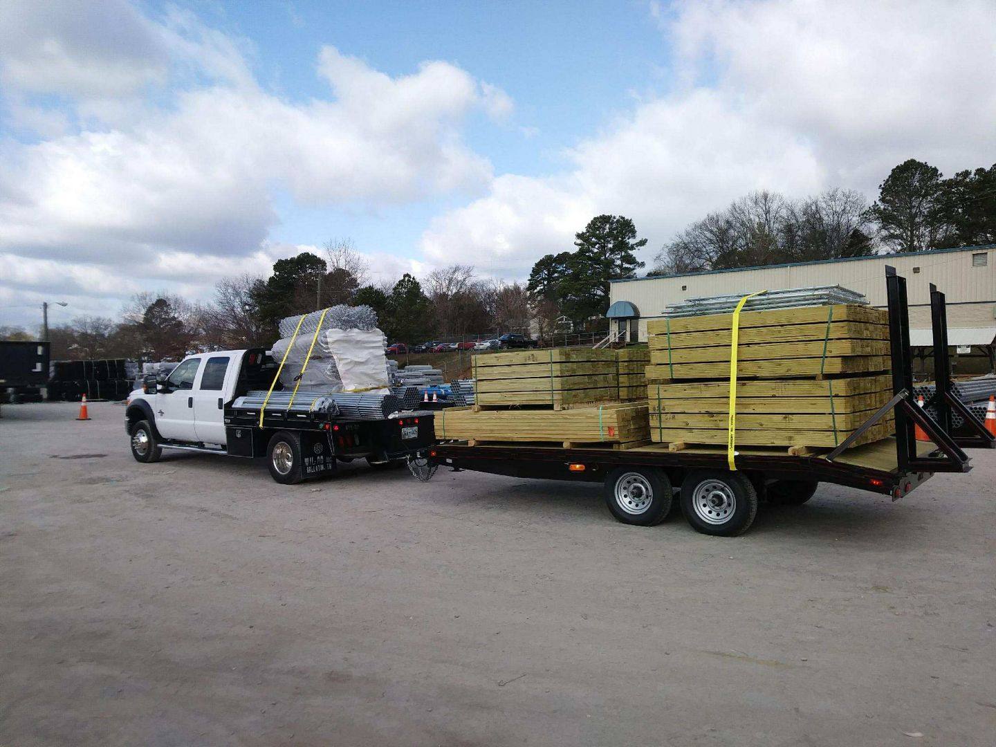 Work truck towing a trailer loaded with fence lumber