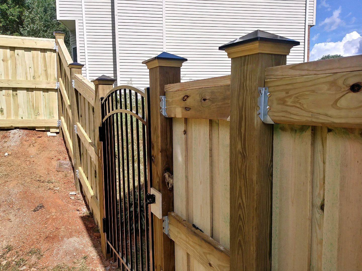 Close view of a wood fence post with a black metal gate and hinges