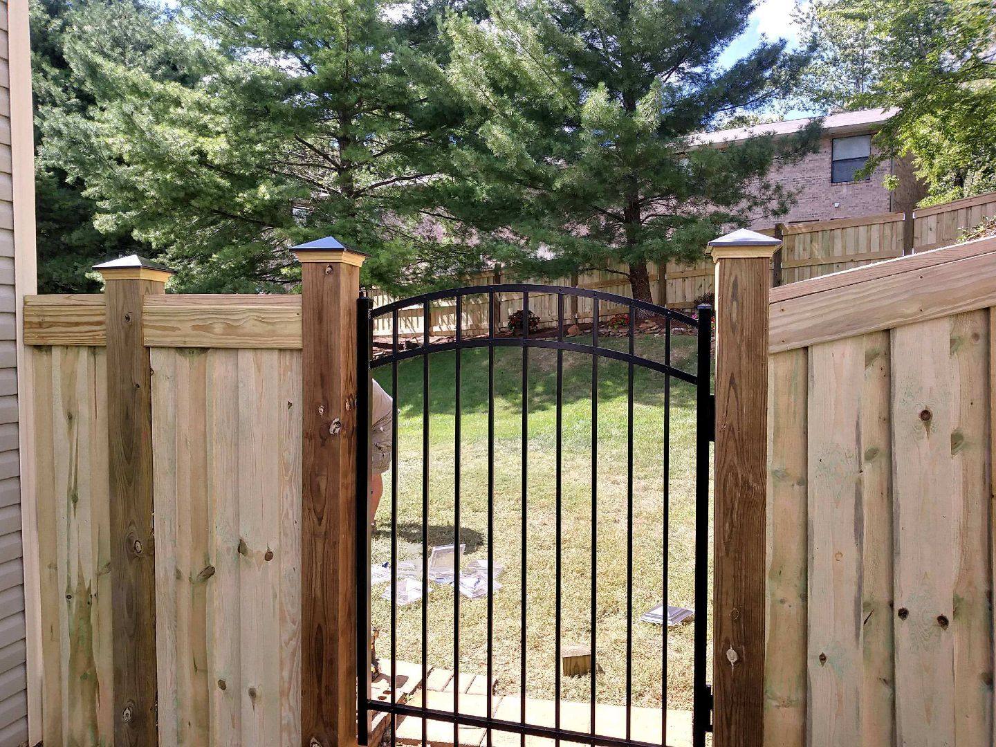 New wood privacy fence with an arched metal gate in a backyard