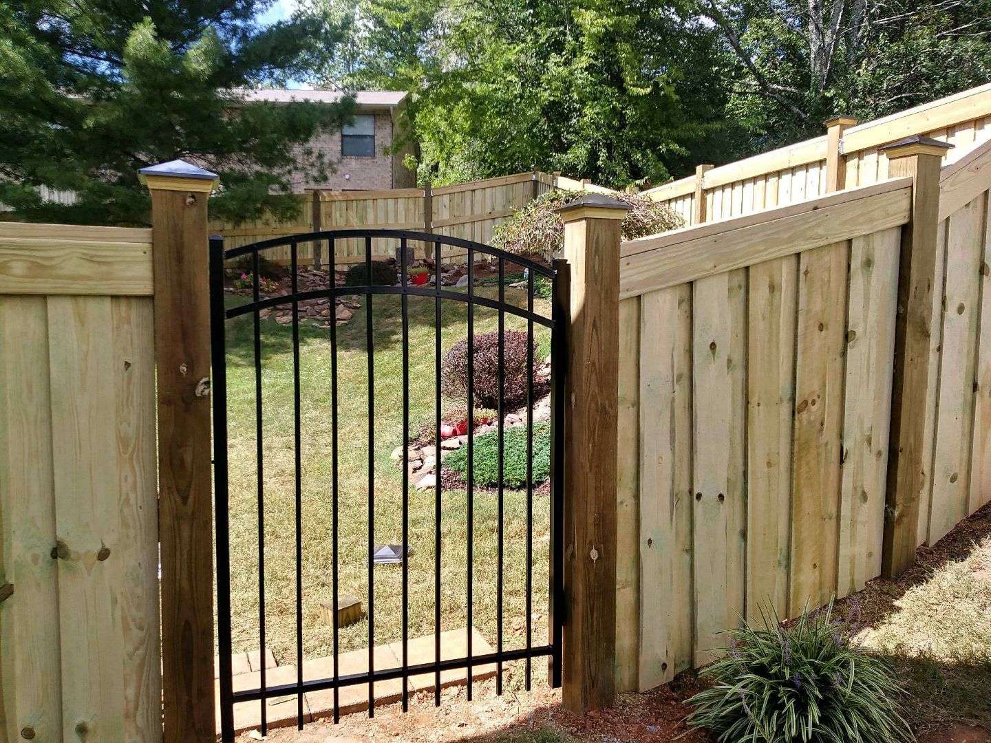 Wood privacy fence with a black arched aluminum walk gate between capped posts