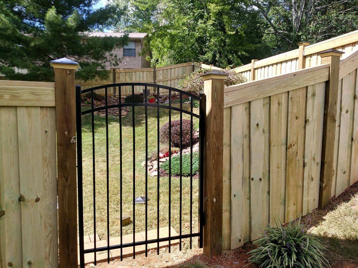 Wood privacy fence with a black arched aluminum walk gate between capped posts