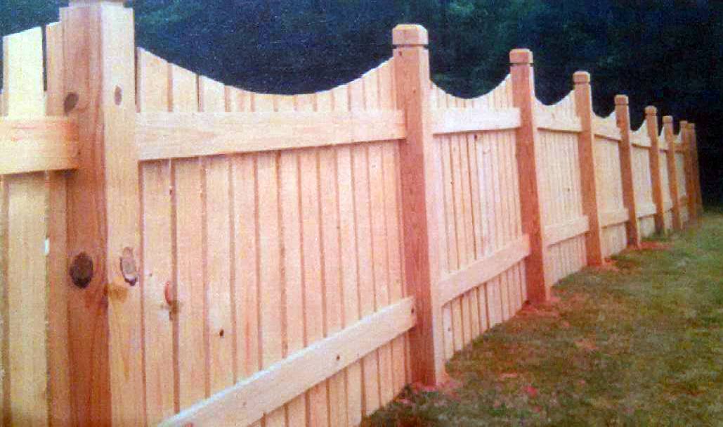 New wood fence with scalloped tops between tall posts